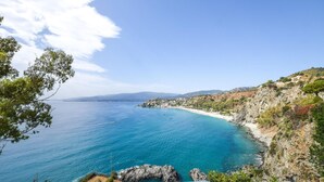 Un paysage côtier avec une mer bleue et limpide, des falaises rocheuses et une plage.
