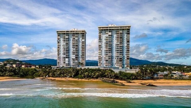 Deux immeubles de grande hauteur, avec une plage et des montagnes en arrière-plan.
