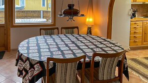 A dining area with a round table covered by a patterned tablecloth, surrounded by wooden chairs with striped cushions.