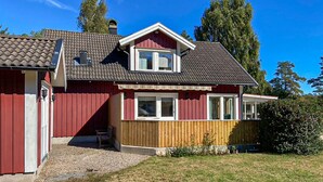 A red house with a grey roof, a wooden deck, and a small porch.