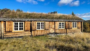 A wooden cabin with multiple windows, situated on a grassy hill with a clear blue sky. - 3 bedroom nice home in Kvam (Kvam)