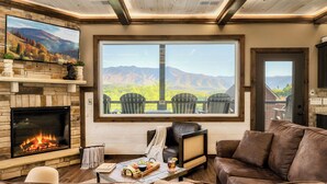 Un salon chaleureux avec une cheminée, un canapé en cuir et une grande fenêtre donnant sur une vue imprenable sur les montagnes.