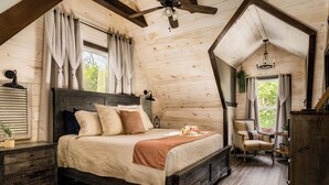 Une chambre confortable avec un plafond en bois, un grand lit, une chaise et une table de chevet.