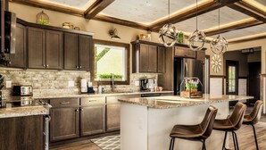 Une cuisine moderne avec des meubles de couleur sombre en bois, un grand îlot central doté de tabourets de bar, des appareils électroménagers en acier inoxydable et un design de plafond original.