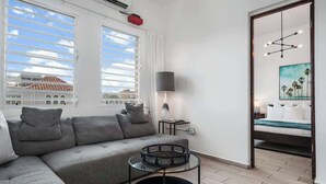 Een moderne woonkamer met een grijze bank, een glazen salontafel en uitzicht op een gebouw door grote ramen.
