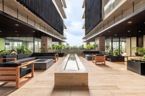 Un área de descanso al aire libre, de estilo moderno, con asientos, una fuente central y abundante vegetación.