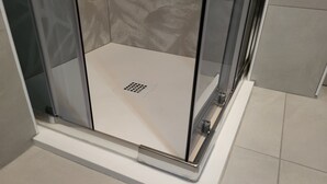 A glass-enclosed shower with a white floor and a drain in the center. - Apartment in front of the hospital  (Modena)