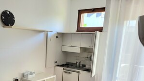 A compact kitchenette with a stove, sink, and cabinets, a small dining table with chairs, and a clock on the wall. - Apartment in front of the hospital  (Modena)