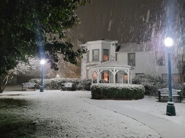 Un mirador en un jardín cubierto de nieve con bancos y un edificio al fondo.