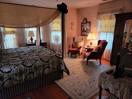 Un dormitorio tradicional con una cama grande, dos sillones, un escritorio y un ventilador de pie.
