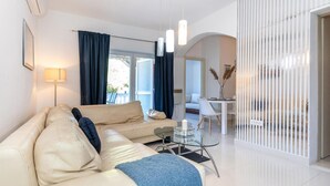 A modern living room with a beige sofa, a glass coffee table, and a dining area with a white table and chairs.