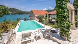 A rectangular pool with lounge chairs and a stone building with a red-tiled roof.