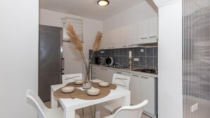 A modern kitchen with white cabinetry, a stainless steel refrigerator, a microwave, and a gas stove. There is a dining table with white chairs and a vase with dried plants.