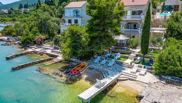 A coastal property with a stone dock, kayaks, and lounge chairs by the water.