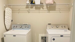 Et vaskerum med to Maytag vaskemaskiner og tørretumblere, et tøjstativ og en hylde med diverse genstande.