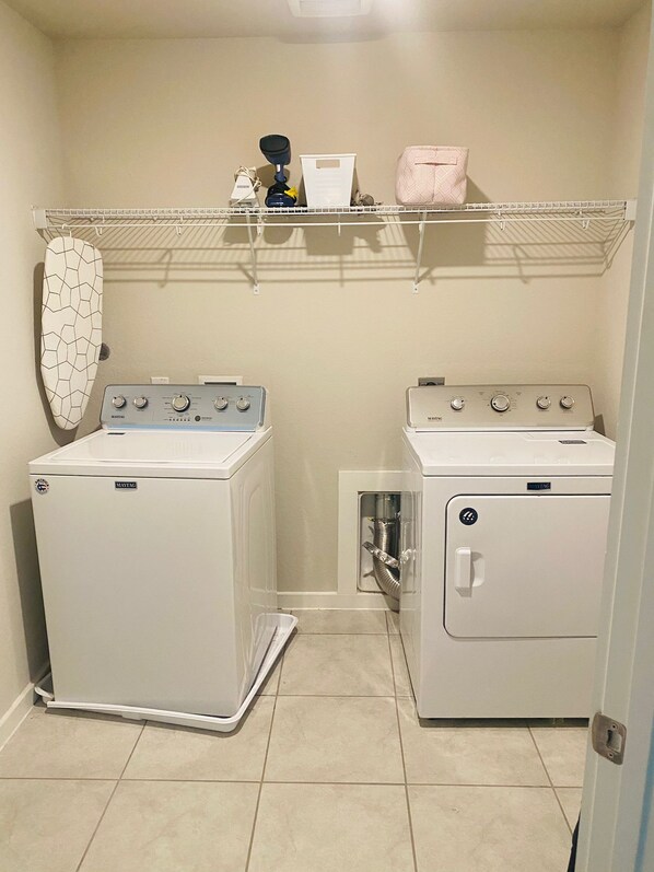 A laundry room with two Maytag washers and dryers, a drying rack, and a shelf with various items.