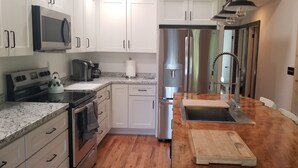 Una cocina moderna con armarios blancos, un refrigerador de acero inoxidable, un microondas, una estufa y un lavamanos.
