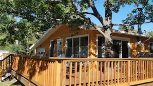 Una cabaña de madera con terraza, ventanas amplias y chimenea.