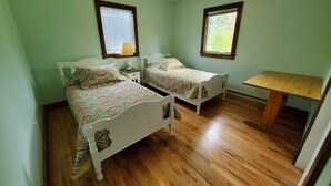 Una habitación con dos camas individuales, una mesa de madera y un ventilador de techo.
