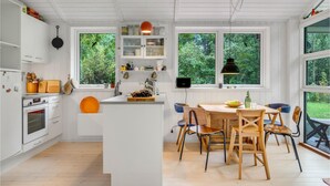 Una cucina moderna con mobili bianchi, un'isola centrale e una zona pranzo con sedie in legno.