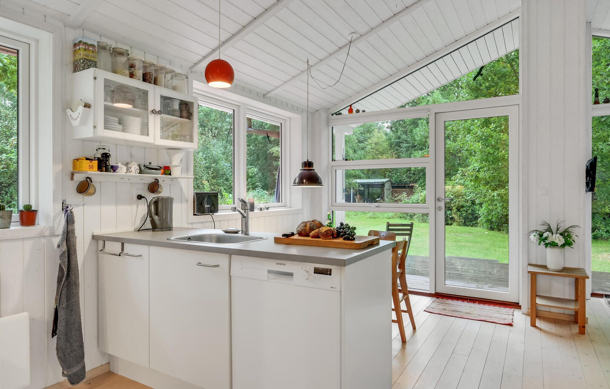 Een moderne keuken met witte kasten, een groot eiland en uitzicht op een weelderige tuin door grote ramen.