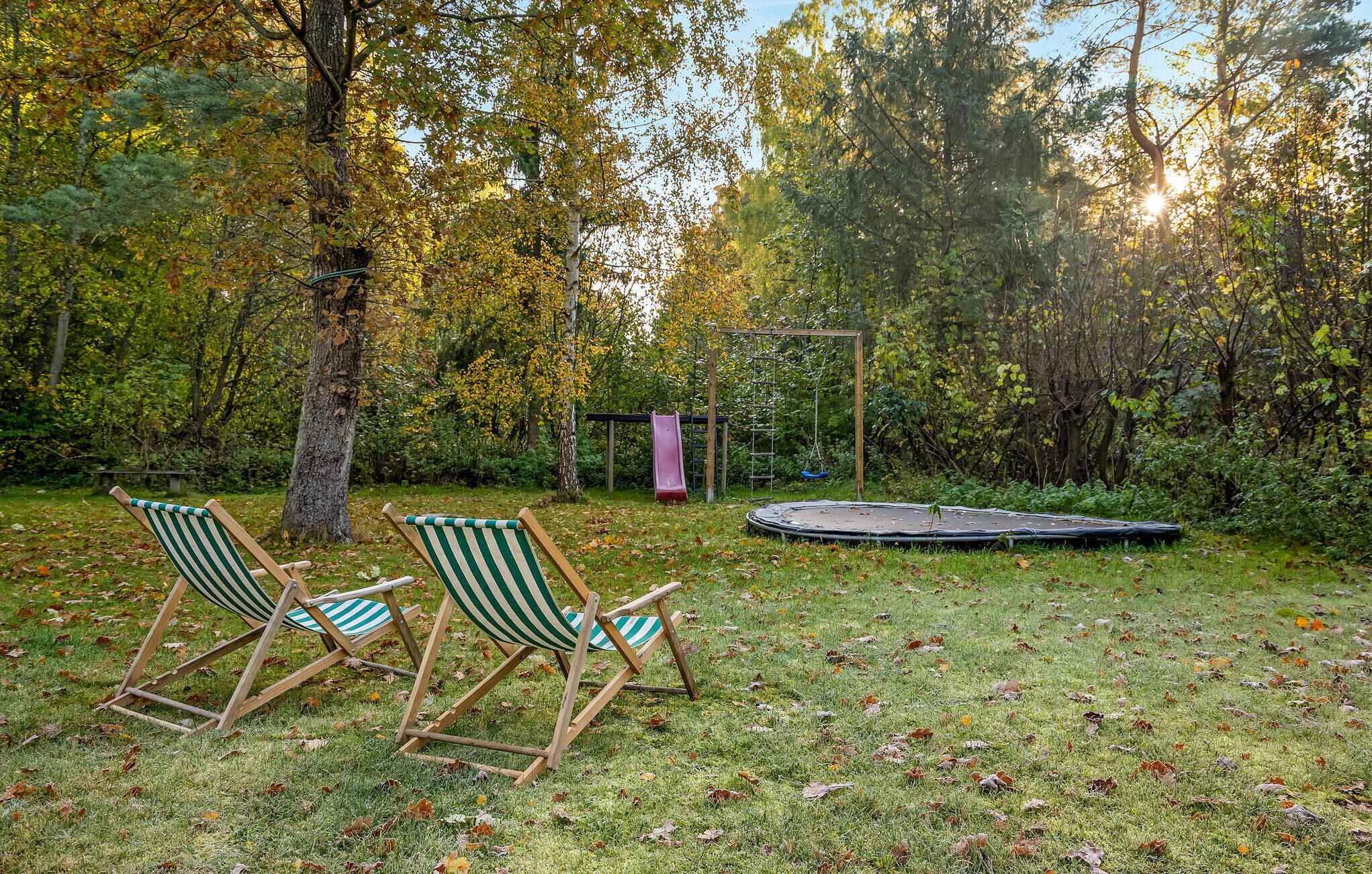Un jardin avec un trampoline, deux chaises de jardin à rayures et une balançoire.