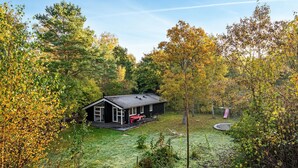 Una baita con veranda, immersa tra alberi e un prato.