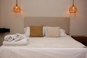 A neatly made bed with white and brown pillows, a folded towel, and two wall-mounted lamps.