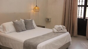 Ein ordentlich bezogenes Bett mit weißer und grauer Bettwäsche, eine Nachttischlampe und gerollte Handtücher auf dem Bett.