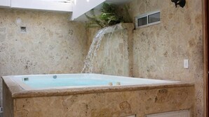 Ein Whirlpool mit Wasserfall, vor einer rustikalen Steinwand.