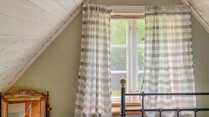 A room with a sloped ceiling, a window with a view of greenery, and a wooden bed frame. - 3 bedroom cozy home in Lärbro (Lärbro)