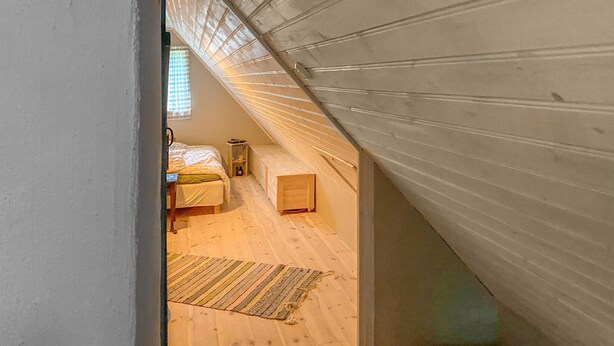 A bedroom with a sloped ceiling, a bed, a bedside table, a small wooden chest, and a window with blinds. - 3 bedroom cozy home in Lärbro (Lärbro)
