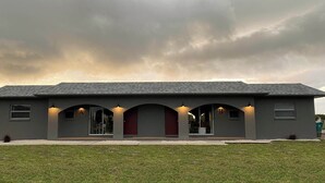 Um edifício de dois andares com telhado plano, varanda frontal coberta com três arcos e uma porta vermelha.