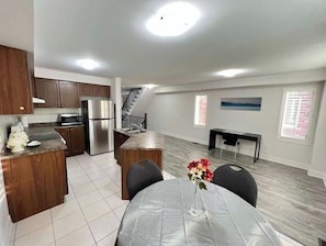 Una cocina moderna con electrodomésticos de acero inoxidable, un comedor con mesa y sillas, y una escalera que conduce a otro nivel.