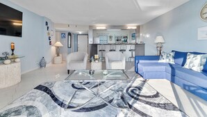 A modern living room with a blue sofa, a glass coffee table, and a patterned rug. - Beautiful Condo on the Beach in Freeport! (Freeport)
