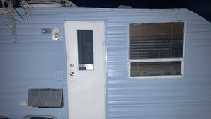 A blue RV with a white door, a small window, and a mounted air conditioning unit. - Retro Rv adorable little romantic paradise (Casselberry)