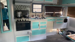 A compact kitchen with teal cabinets, a stove, and a sink. - Retro Rv adorable little romantic paradise (Casselberry)