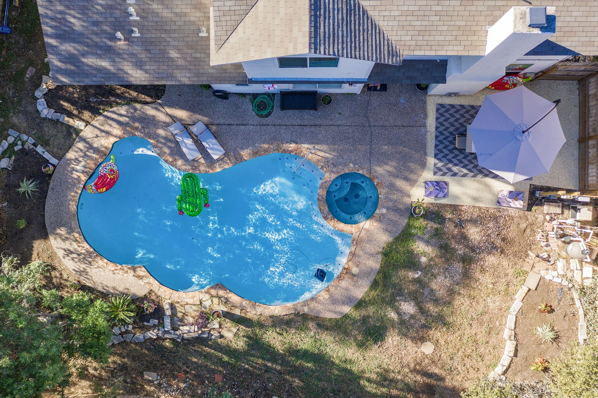 An aerial view of a backyard with a swimming pool, a hot tub, and a patio area with umbrellas.
