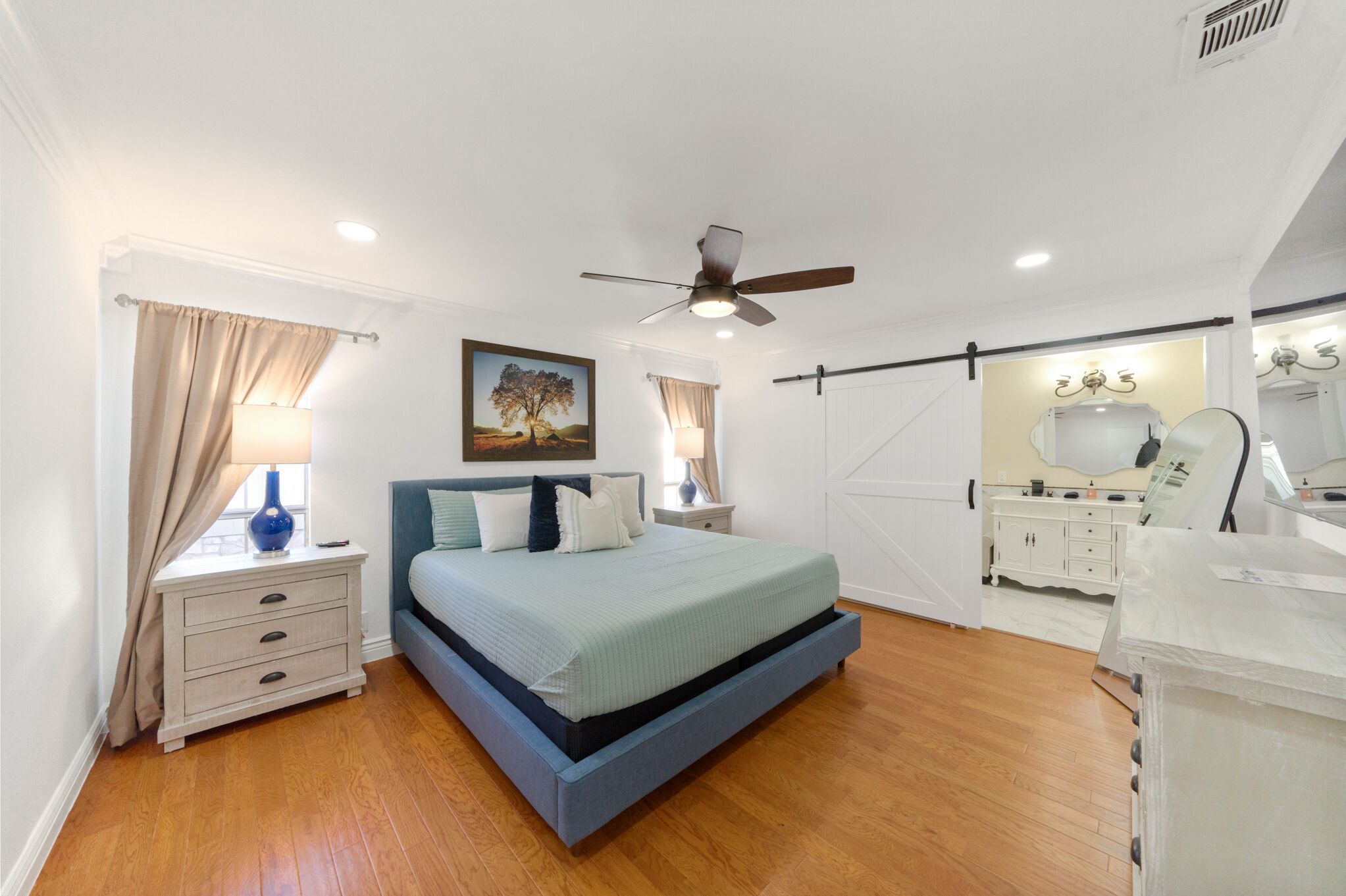 Una camera da letto con un letto, comodini, una cassettiera, una ventola a soffitto e un quadro appeso al muro.