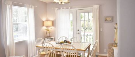 A dining area with a wooden table and white chairs, a chandelier, and a view through a glass door.