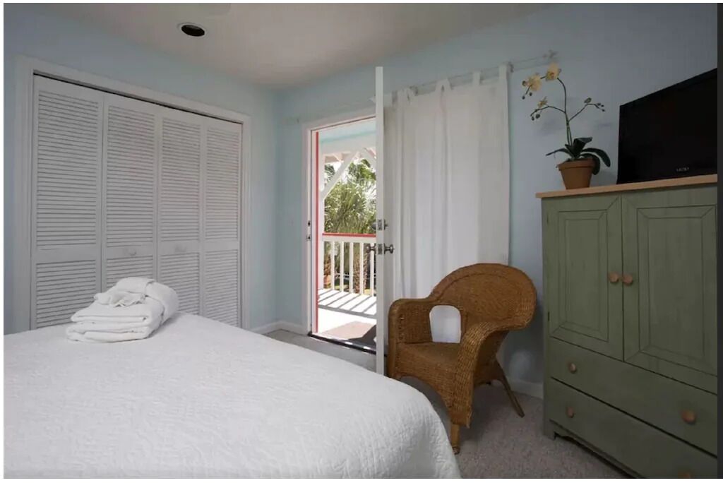 A bedroom with a bed, a wicker chair, a green cabinet, and a television on a stand.