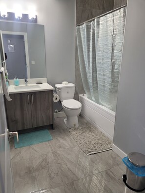 A bathroom with a toilet, sink, and shower curtain. - New 2-bedroom legal basement in Calgary (Calgary)
