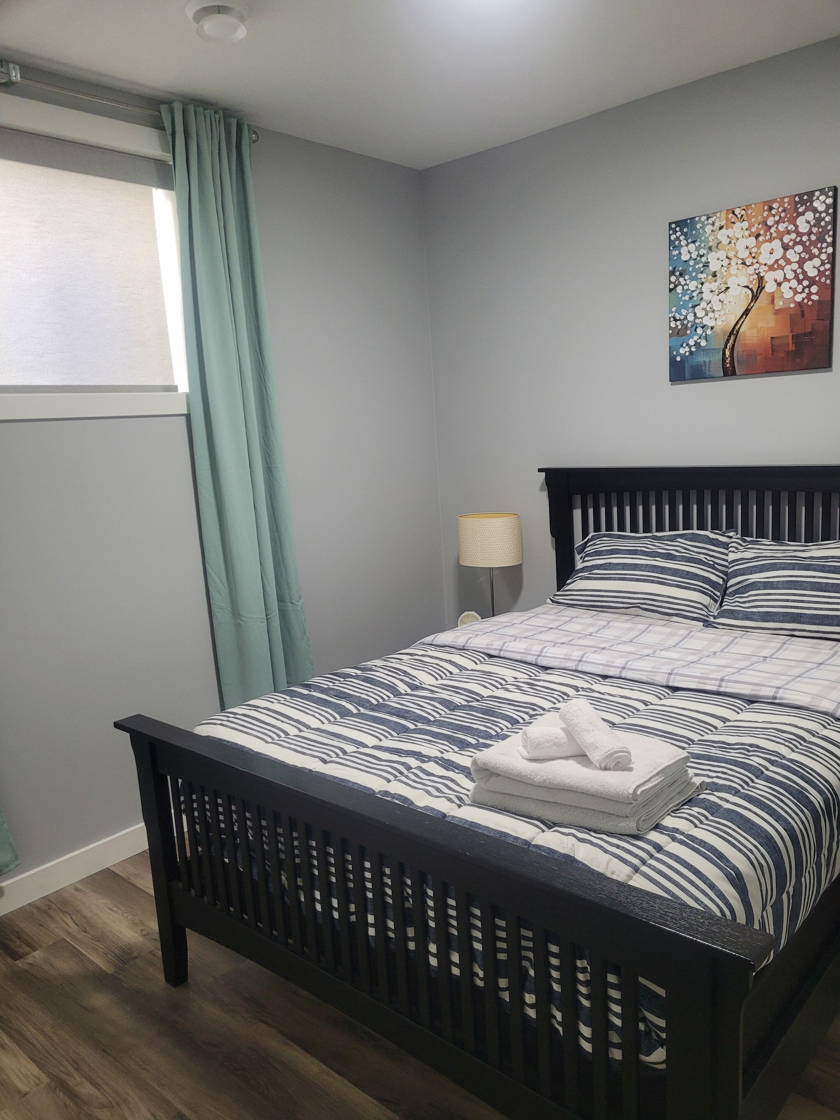 A neatly made bed with striped bedding, a nightstand with a lamp, and a wall painting.