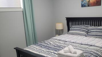 A neatly made bed with striped bedding, a nightstand with a lamp, and a wall painting.