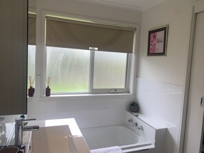 Bathroom features a large bathtub, sink, and window with a blind.