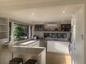 A modern kitchen with a central island, built-in shelves, and a view of greenery outside. - Large house in beautiful setting on Portarlington wetlands (Portarlington)