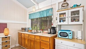 A kitchen with wooden cabinets, a white countertop, a blue microwave, and a hanging light fixture. - Peaceful Mountain Retreat- Jungle Mountain Vibes (Holualoa)