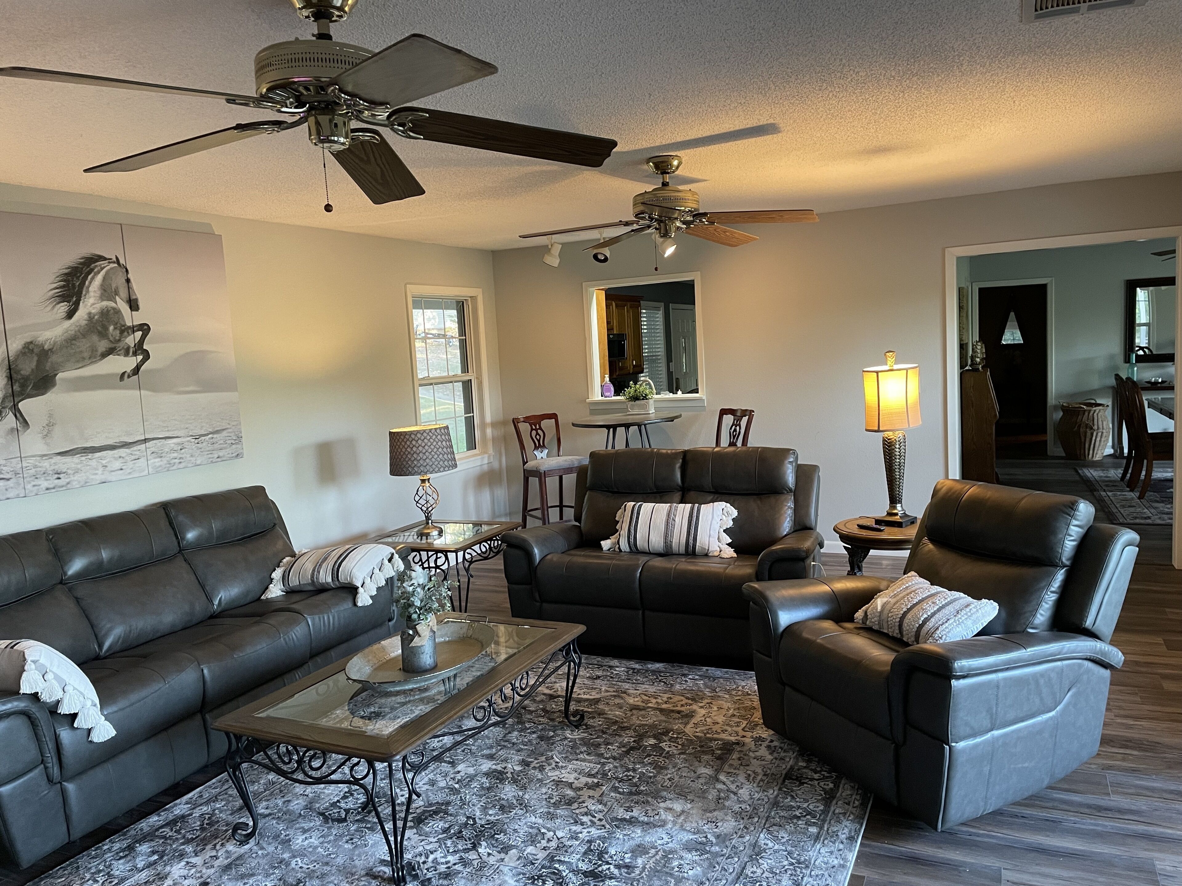 A living room with leather sofas, a coffee table, and two ceiling fans.