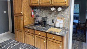 A kitchen with wooden cabinets, a marble countertop, a coffee maker, and a brick backsplash. - Lake Hamilton, BoatHouse, Hot Tub, 
Barge Rental, Sleeps 10, H.S. National Park (Hot Springs)
