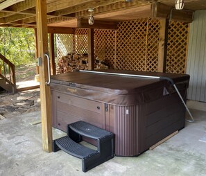 Ett bubbelbadkar med en inbyggd trappsteg, placerat under en träpergola med ett spaljéliknande bakstycke.